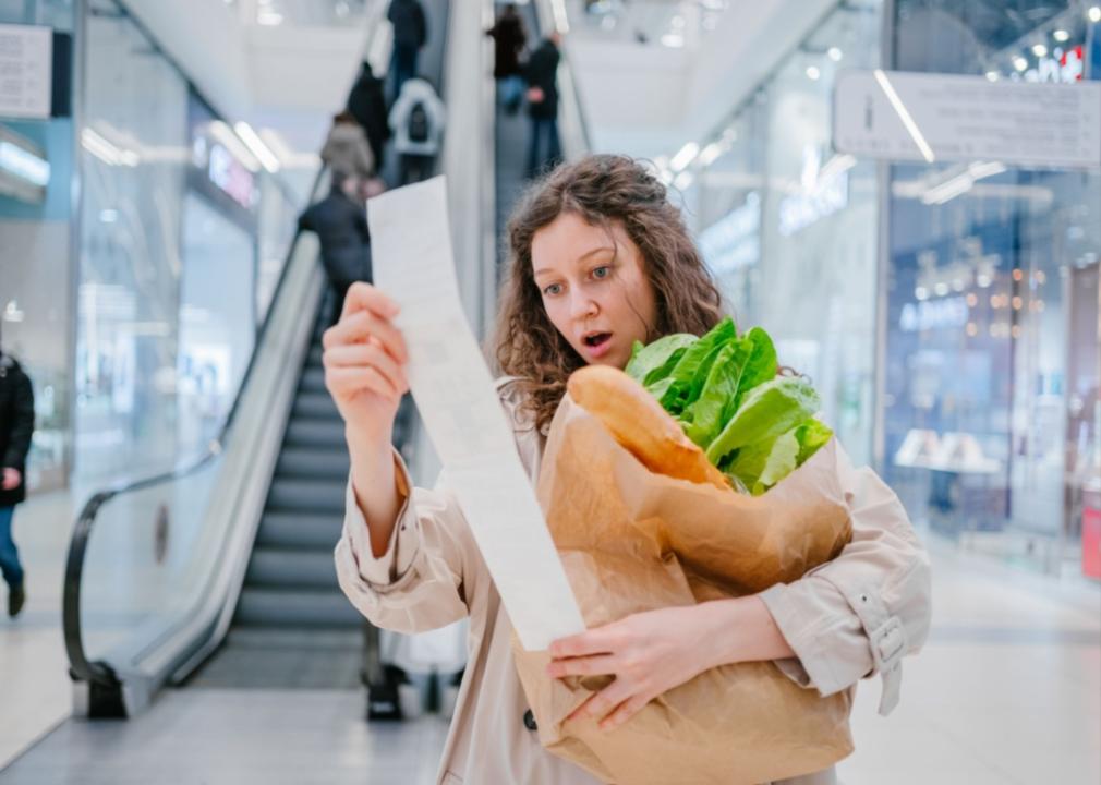 A woman looking surprised at a grocery receipt.