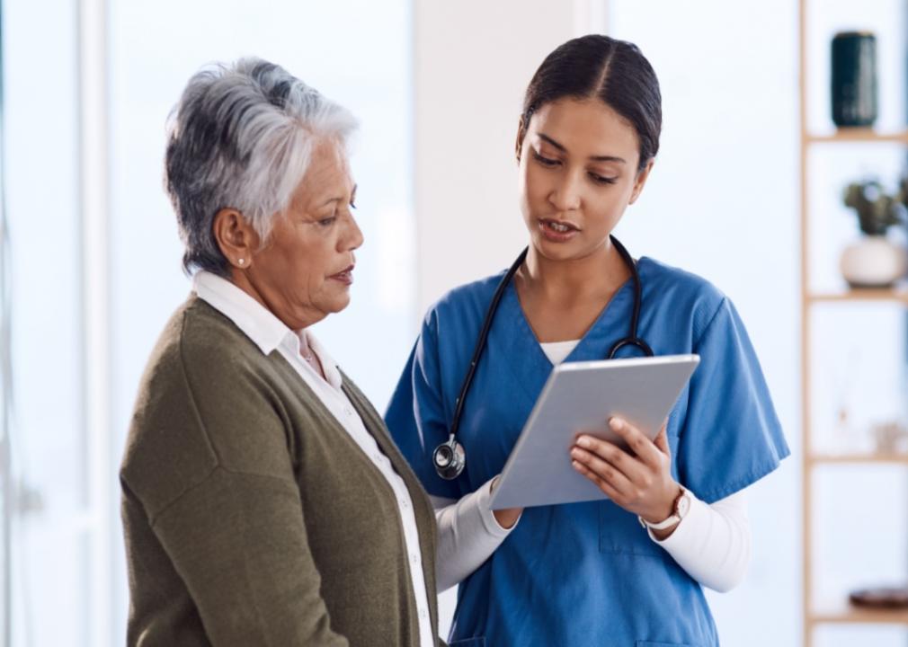 A health care worker holding a tablet while talking to a patient.