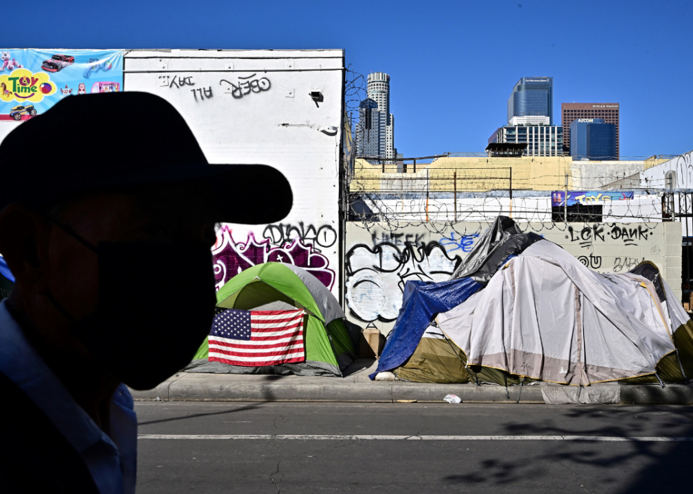 A man walking in front of a homeless encampment.