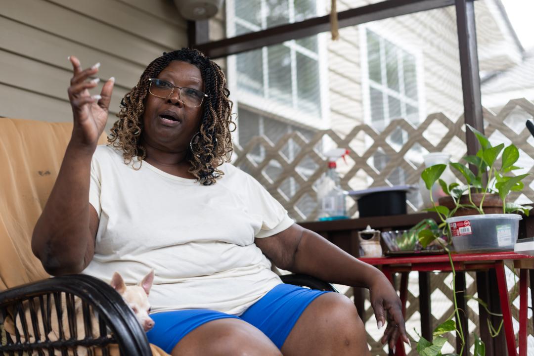 Luvenia Brown, a Black woman, sitting on her porch in next to a small white dog, lives in Rosemont, on a street that floods repeatedly. “If the water continues rising the way it is, I don’t want to be here,” she says.