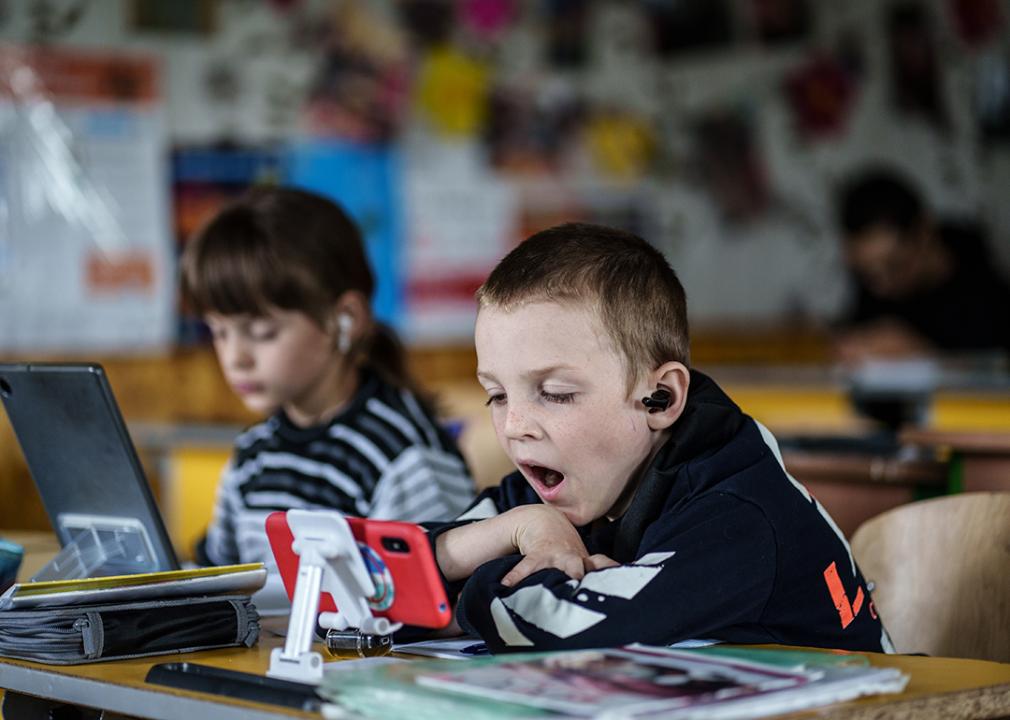 Two young children in a community center using tablets and smartphones for an online class.