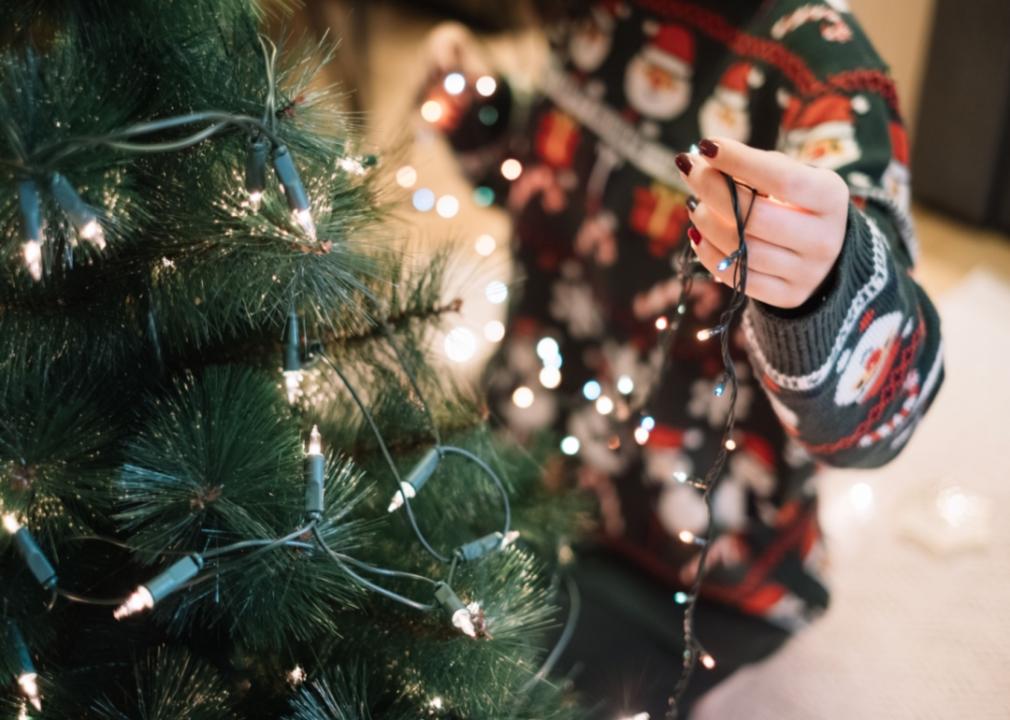 A woman putting lights on a Christmas tree.