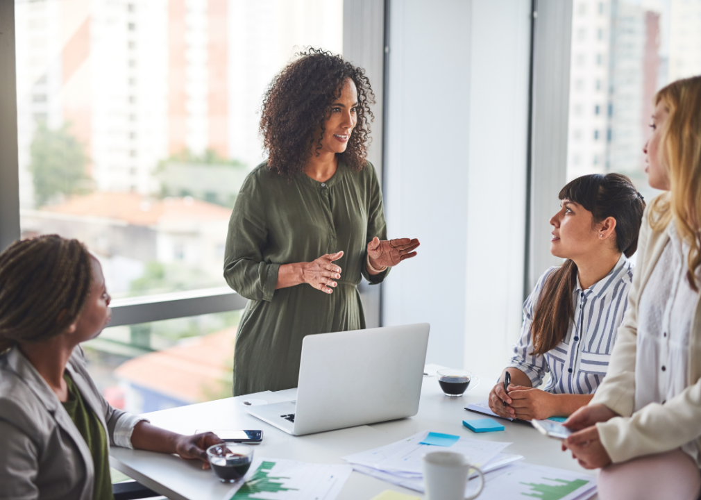 A manager positively talks to three other women in a meeting in a brightly lit office.