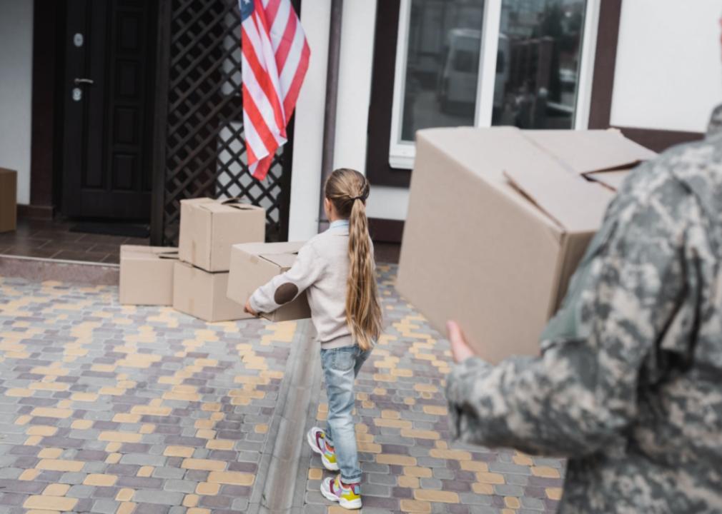A man in camo and a young girl moving boxes into a house.