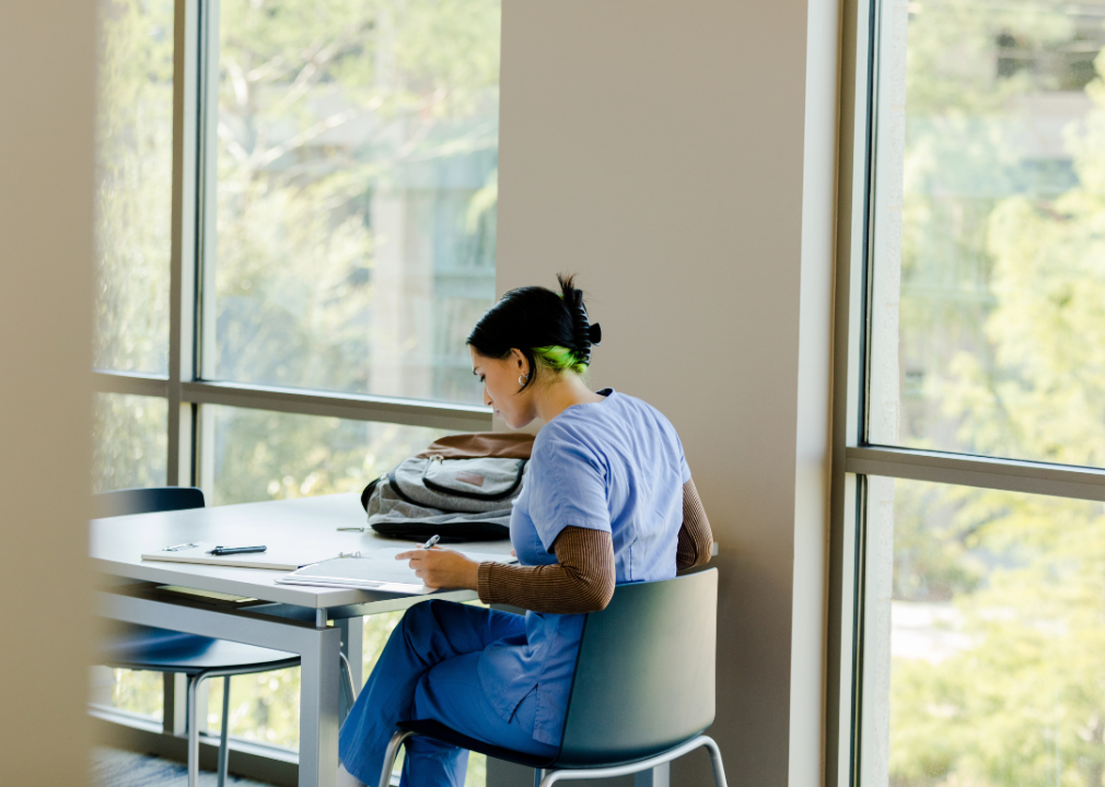 A woman in blue scrubs doing paperwork at a table.