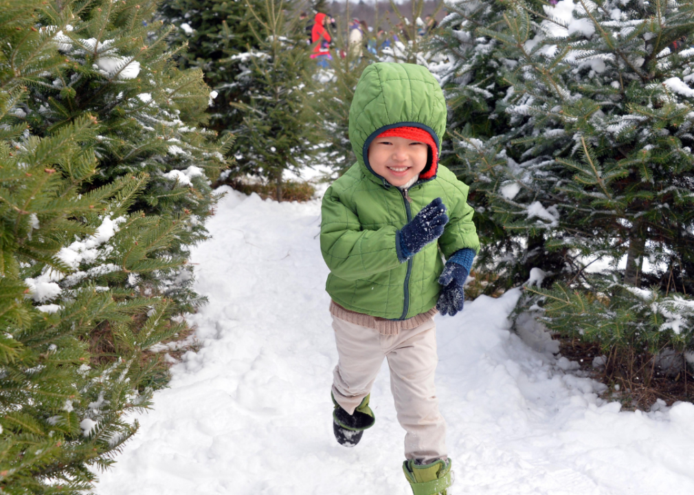 A happy child running through a snowy tree farm.