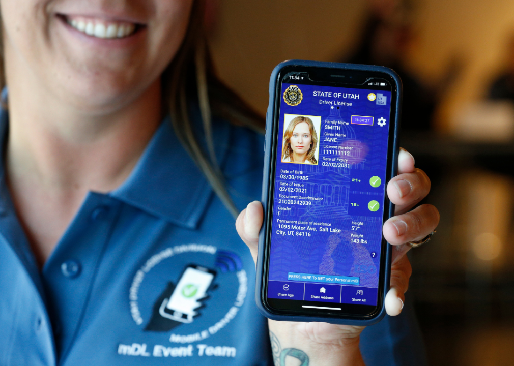 A person wearing a polo shirt with an mDL Event Team logo holds up a smartphone with a digital State of Utah driver license for a Jane Smith.