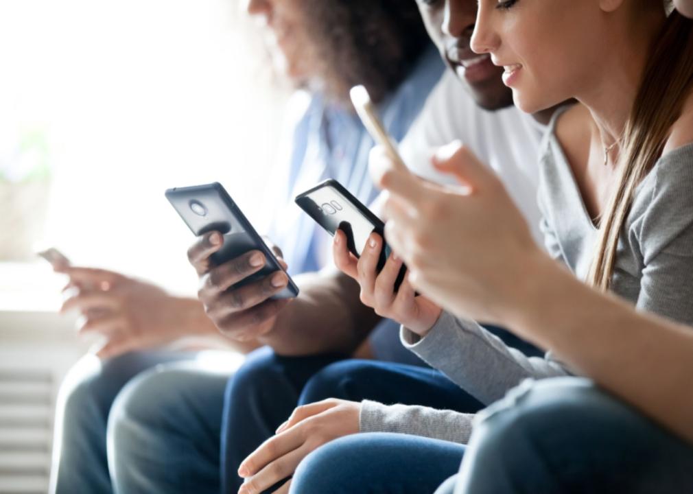 Several people sitting in a row, all on their smartphones.
