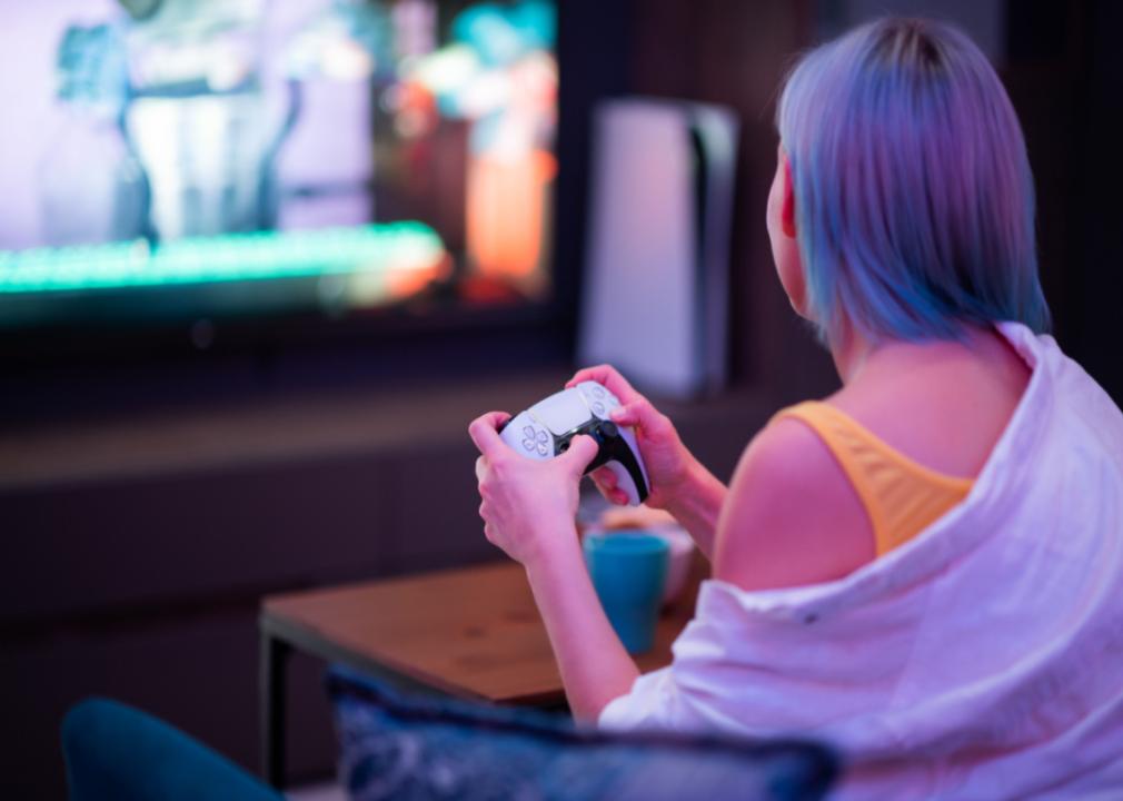 A teen with blue and purple hair playing a Playstation 5.