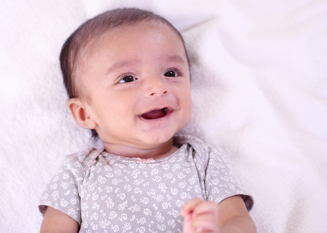 Smiling baby lying on back on white blanket.