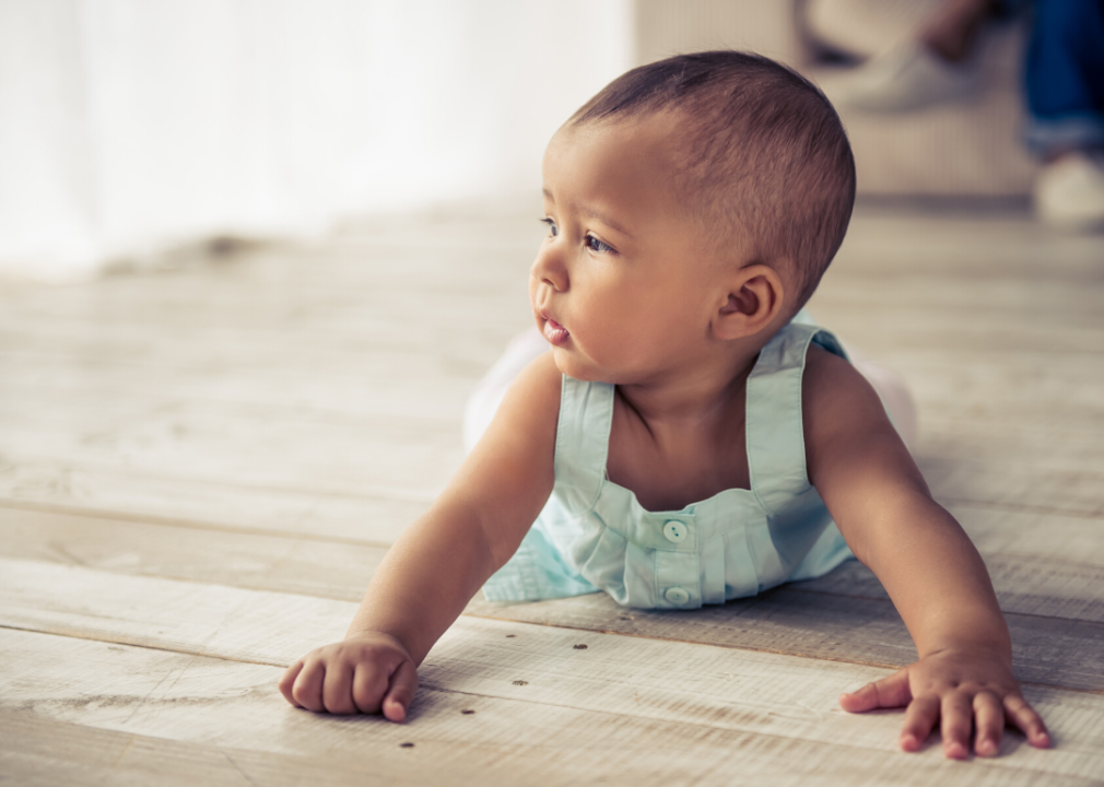 Baby girl crawling on wooden floor.