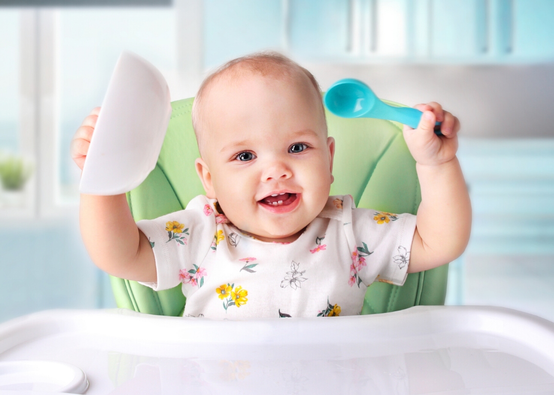 Baby sitting in high chair, holding bowl and spoon.