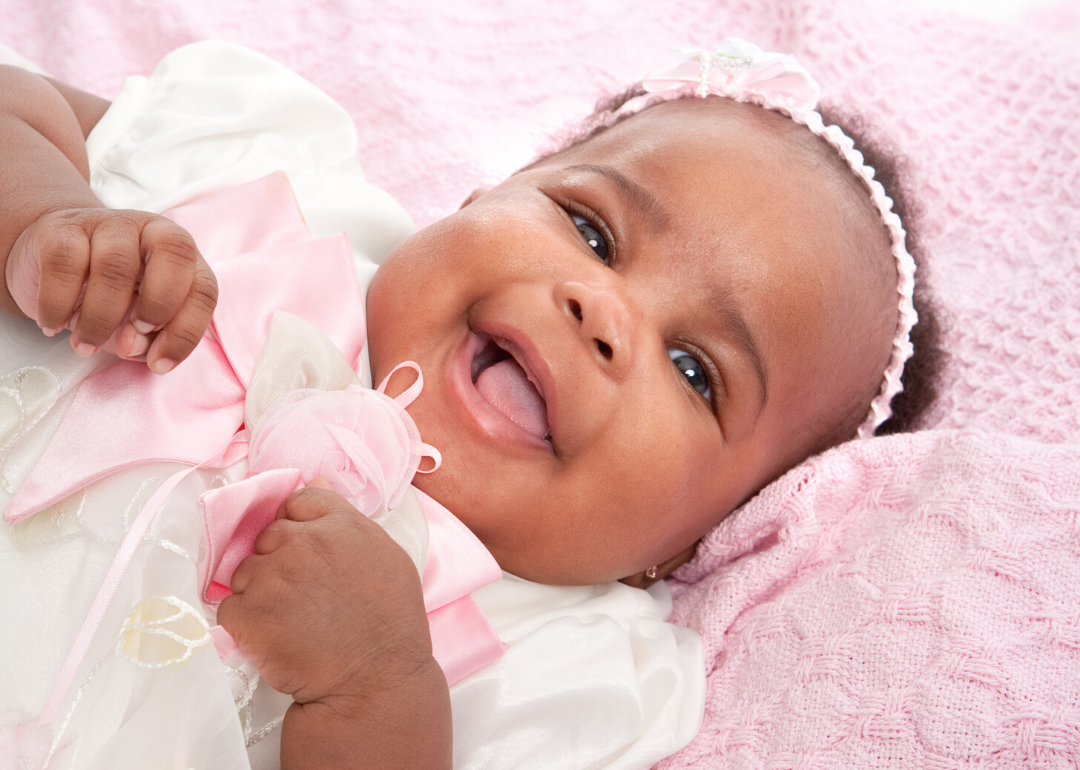 Smiling baby wearing pink headband laying on pink blanket.