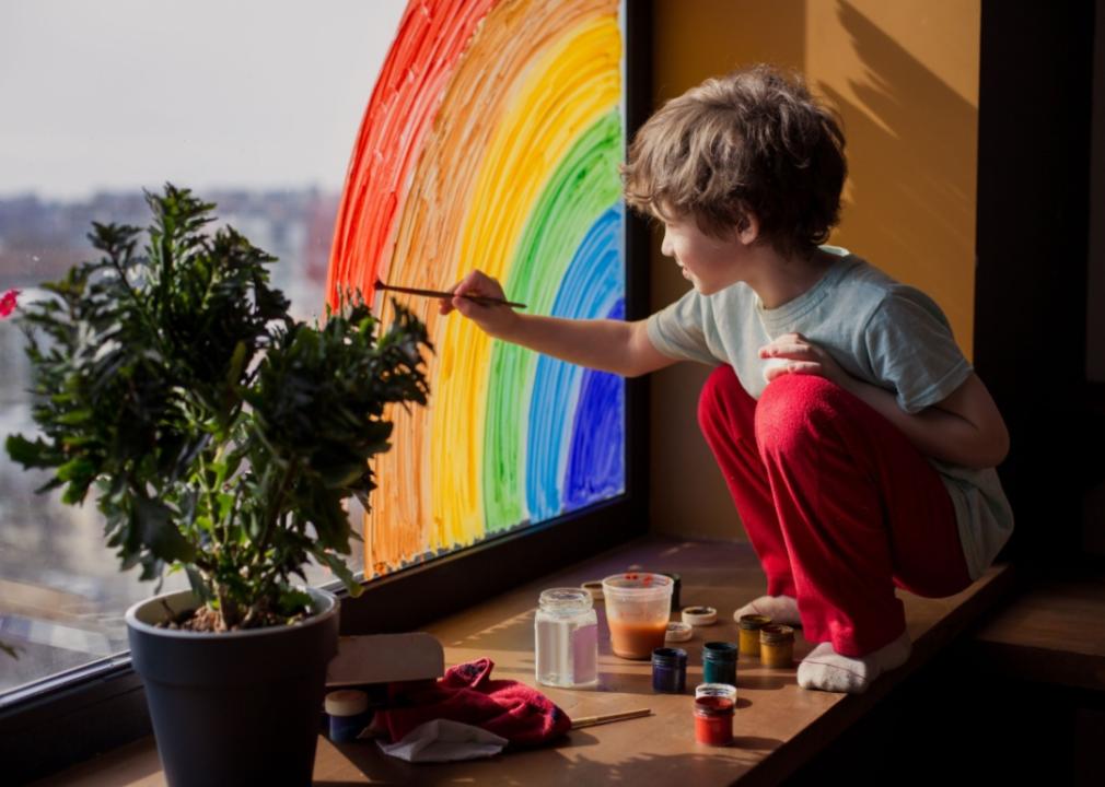 A child painting a rainbow on a window.