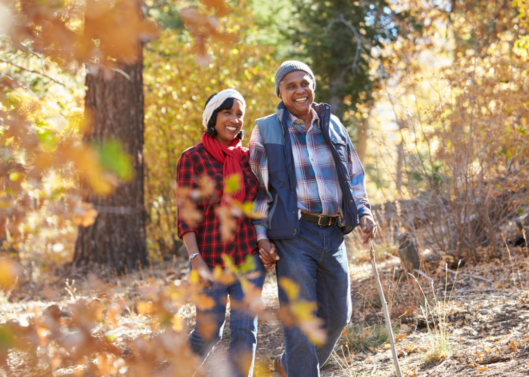 A happy retired couple walking on a trail in a wooded area during autumn. 