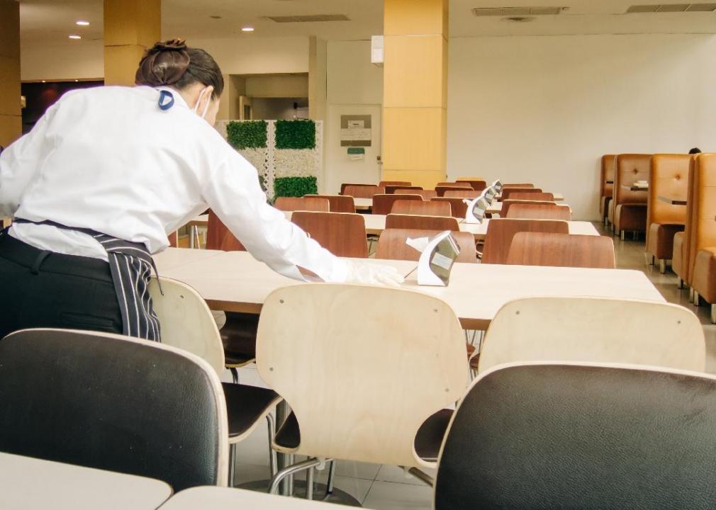 A person wiping down a cafeteria table. 