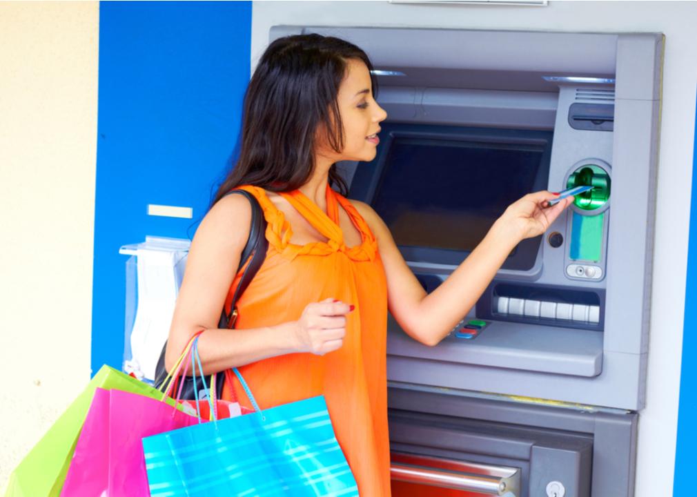 A young woman at the ATM carrying colored shopping bags 