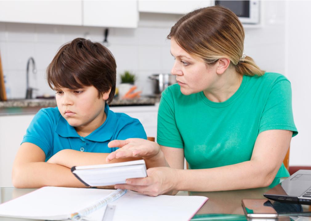 A child refuses to look at the homework his mother holds up to him