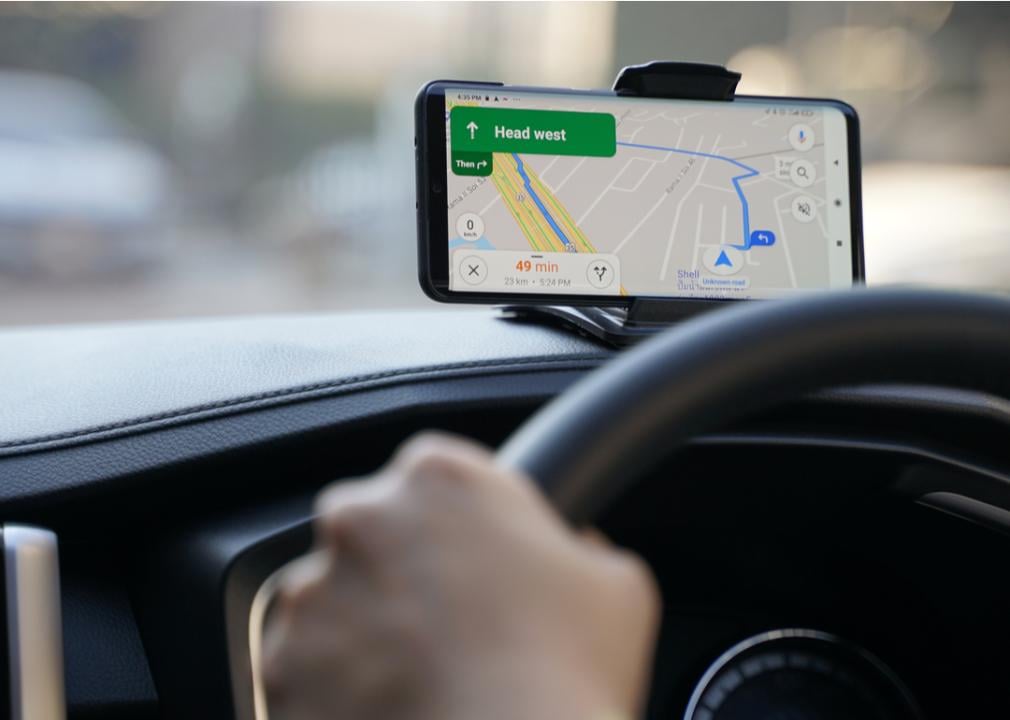 A man driving a car and holding a smartphone open to a GPS application