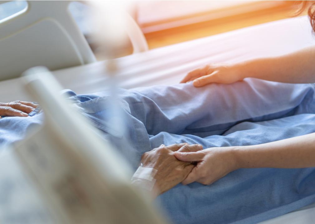 A caregiver and elderly senior patient holding hands in a nursing hospice