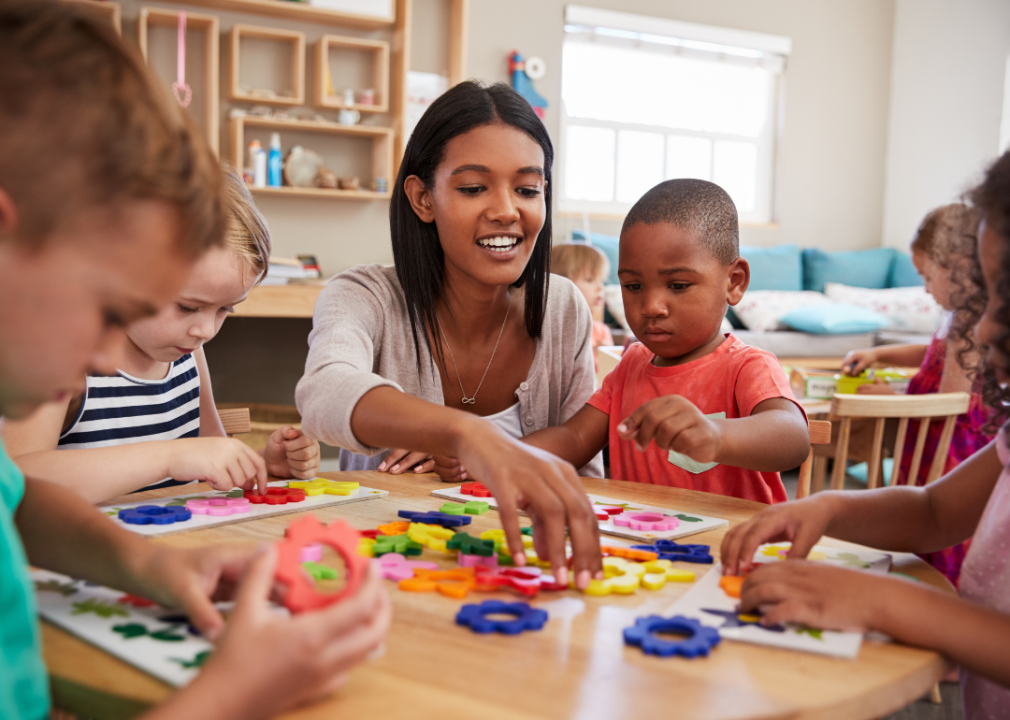 A teacher working with young students at a table in a classroom.