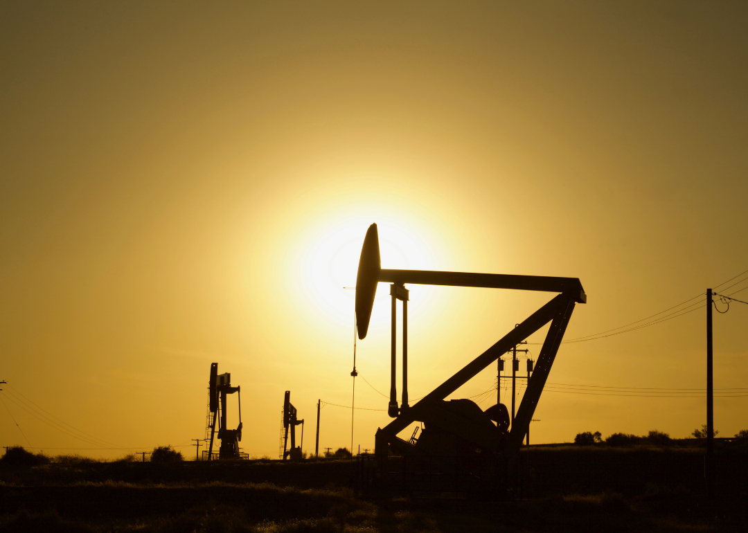 The sun shines behind an oil derrick.