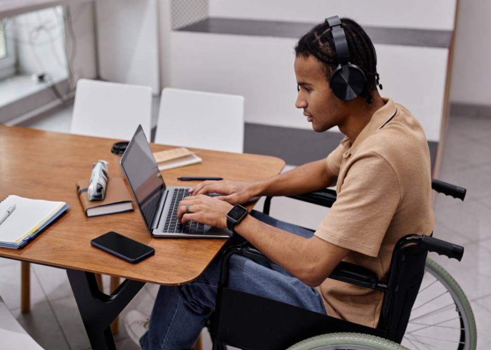 A man in a wheelchair using headphones at a laptop.