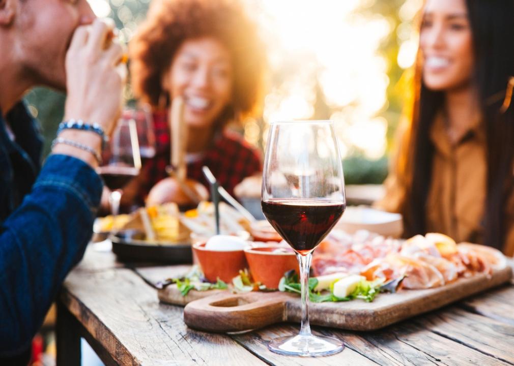 A wine glass on a table of food with people laughing in the background.