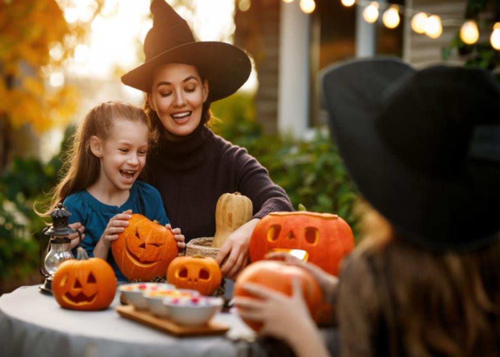 A woman dressed as a witch helping kids decorate pumpkins.