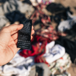 Hand holding clothing tag with textile waste in background.