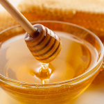 Closeup honey dripper, glass bowl of honey, and honeycomb.