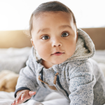 Brown eyed baby wearing fleece hoodie looking into camera.