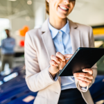 Woman in car dealership looking at tablet.