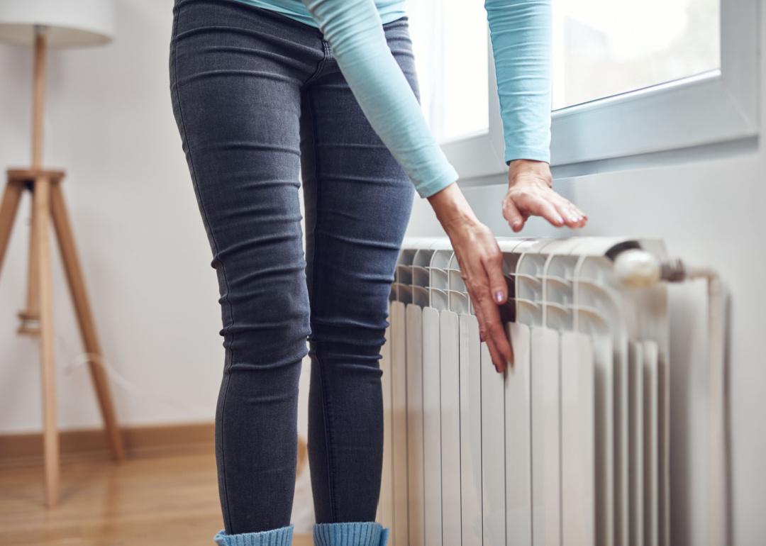 Woman checking radiator heat on winter day.