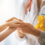 Doctor with yellow childhood cancer awareness ribbon holding child’s hands.