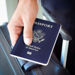 Hand holding U.S. passport and wheeling a suitcase.