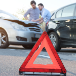 Two men standing by car crash with red emergency triangle on road.