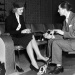 Shoe salesman helping woman try on a pair of high heels in the 1930s