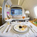 Emirates airlines first class suite with a large screen, a mini bar, and a table set with a meal and a drink in a glass flute.