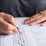 Hand with pencil filling out standardized test form.