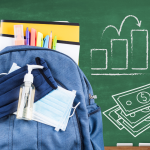 Backpack with face mask and sanitizer in front of chalkboard showing a graph and dollar bills.