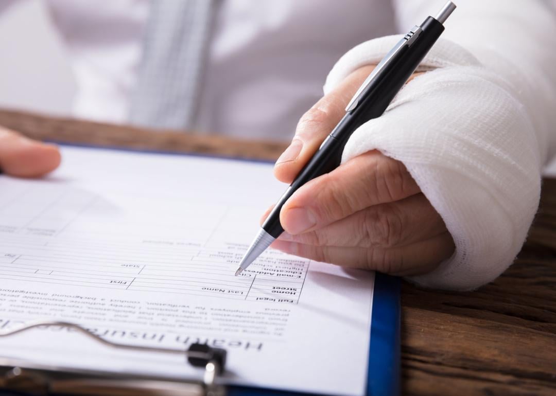 Person with bandaged hand filling out claim form.