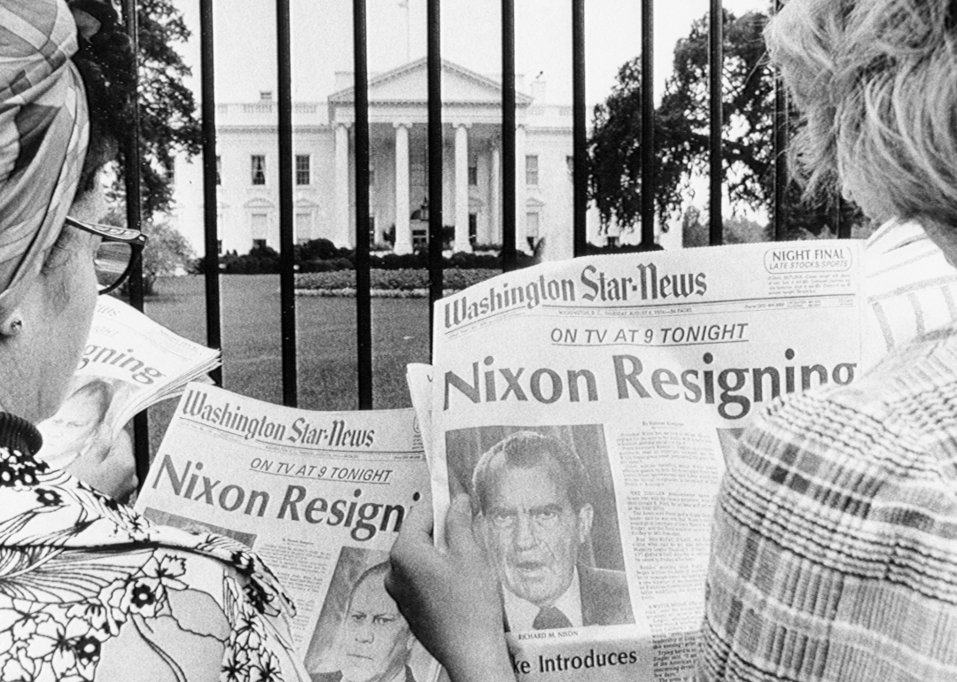 Tourists reading newspapers with Nixon resignation headline in front of the White House.