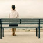 Woman sitting alone on a bench, looking out to the sea.