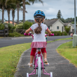 Young girl with braid and helmet riding bike with training wheels in warm weather state