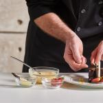 Closeup of private chef in black chef's coat assembling dessert.