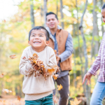 A young boy, his older sister, and his father play in the leaves in the woods