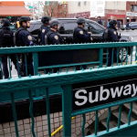 Photo of a subway sign with police officers behind it