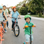 Mother, father, daughter, and son ride bikes and scooter in a suburban neighborhood.