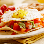 Plate of huevos rancheros, with tortilla, salsa, and egg, sitting on a yellow napkin.
